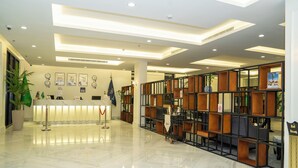 A hotel reception area with a marble floor, a reception desk, a seating area with sofas, and a wall with framed pictures and a flag. - BRAI HOTEL (Al Duwadimi)