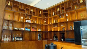 A wooden bar area with shelves containing bottles, glasses, and kitchen appliances. - BRAI HOTEL (Al Duwadimi)