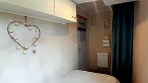 Et aflangt rum med en seng, en lampe i hjerteform, et håndklædestativ og en radiator.
