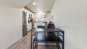 A modern kitchen with white cabinets, stainless steel appliances, and a dining area with a black metal table and chairs. - Mtn View Getaway - w/ Hot Tub, Close to Schweitzer (Kootenai)