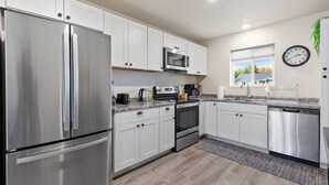 A modern kitchen with stainless steel appliances, white cabinetry, and a window with a view. - Mtn View Getaway - w/ Hot Tub, Close to Schweitzer (Kootenai)