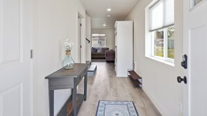 A narrow hallway with a wooden floor, white walls, and a door on the left. A small table with a vase of flowers is on the left side. - Mtn View Getaway - w/ Hot Tub, Close to Schweitzer (Kootenai)