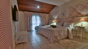 A bedroom with two beds, a small table, a TV mounted on the wall, and a window with curtains.