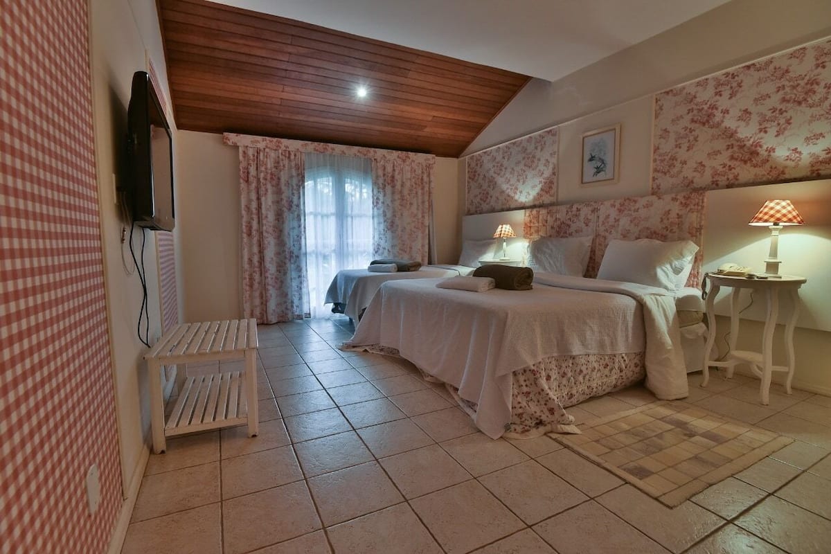 Ein Schlafzimmer mit zwei Betten, einem kleinen Tisch, einem an der Wand montierten Fernseher und einem Fenster mit Vorhängen.