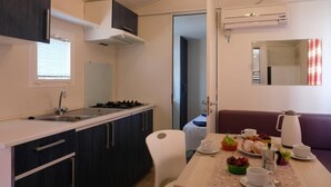 Una cocina compacta con lavabo, estufa y armarios, un comedor con una mesa preparada para el desayuno, y un sofá.