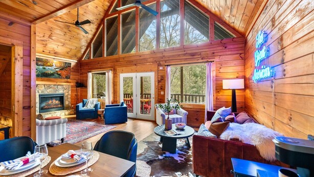A spacious cabin with a high ceiling, large windows, a fireplace, and a dining area with a table set for four.