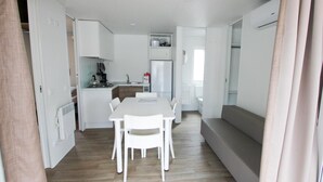 A compact kitchen with white cabinetry, a dining table with chairs, and a built-in bench. - Torre Rinalda Beach Camping Mobilehome Happy Superior for 6 people (Lecce)