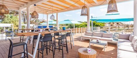 An outdoor patio with wooden tables, chairs, and a sofa.