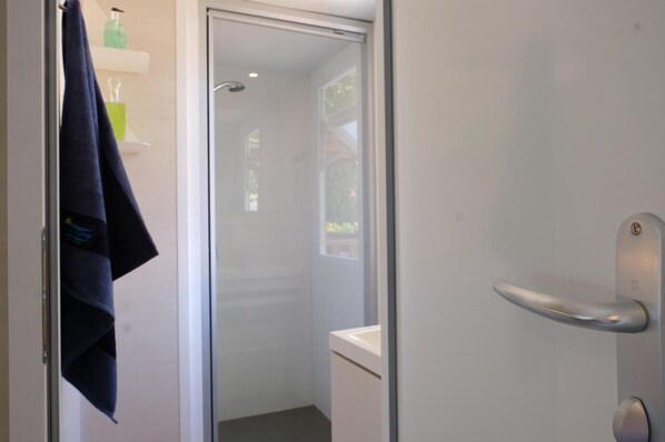 Un baño moderno con puerta de vidrio para la ducha, un lavamanos blanco y una toalla colgada en la puerta.