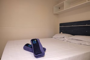 A hotel room with a neatly made bed, a headboard, and a shelf above the bed.