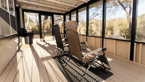 A covered outdoor seating area with two chairs and a trash can.
