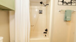 A bathroom with a bathtub, a shower curtain, a towel rack, and a wall-mounted light fixture.