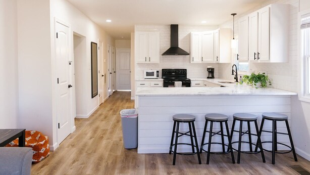 Une cuisine moderne avec des meubles blancs, un îlot central doté de tabourets, une cuisinière noire et un four à micro-ondes.