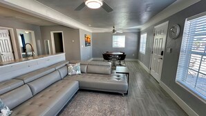 A modern living room with a sectional sofa, a dining table with chairs, and a ceiling fan. - Lil Lavender House in Fort Myers Beach (Fort Myers Beach)
