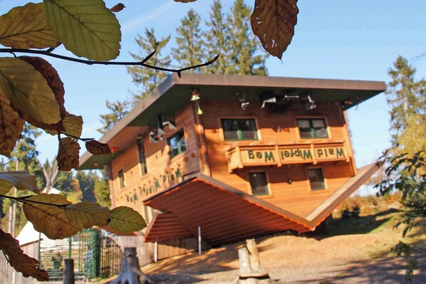 A wooden cabin with a slanted roof and a sign that reads "Wald Wiese."