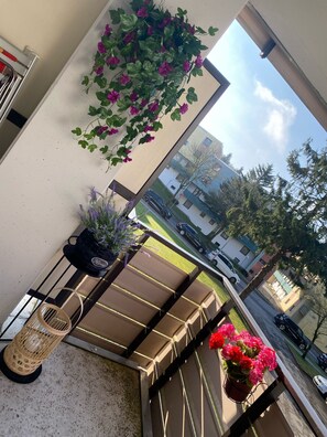 Enjoy the street view from this balcony with a hanging plant, wicker chair, and comfortable bench.