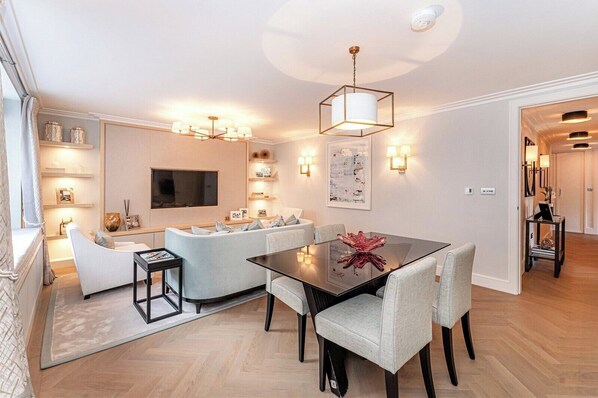 A modern living room with a sofa, a dining table, and a TV mounted on the wall.