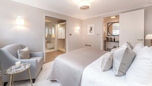Ein Schlafzimmer mit einem Bett, einem Sessel, einem kleinen Tisch, einem Kleiderschrank und einem durch eine offene Tür einsehbaren Badezimmer.