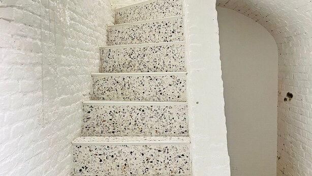 A spiral staircase with white walls and speckled steps.