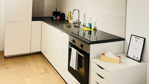 A modern kitchen with white cabinets, a black countertop, stainless steel sink, and a built-in oven. There is a welcome sign on the wall and a small table with a box and a bottle.