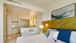 Une chambre d’hôtel avec un grand lit, une salle de bain avec une baignoire, un miroir et un tableau au mur.