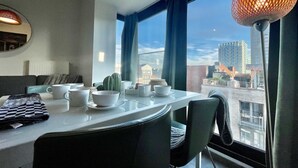 A modern dining area with a view of the cityscape through large windows, a table set with white dishes, and a unique spherical lamp. - Cozy 1BR City Centre Near Meir Shopping by Oneluxstay (Antwerp)