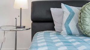 A neatly made bed with a patterned bedspread, a black upholstered headboard, and a bedside lamp.