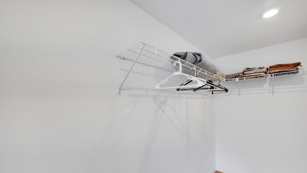 A room with a white wall, a wooden floor, and a ceiling-mounted drying rack with clothes.