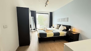 Une chambre à coucher avec un lit, une table de chevet, une lampe et une vue sur l’extérieur.