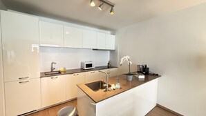 A modern kitchen with white cabinets, a stainless steel sink, a microwave, and a small island with a potted orchid. - Spacious 3BR 2/5 BA Near Diamond District by Oneluxstay (Antwerp)