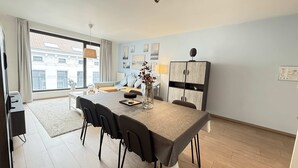 A modern living room with a dining area, large windows, and a view of buildings. - Spacious 3BR 2/5 BA Near Diamond District by Oneluxstay (Antwerp)
