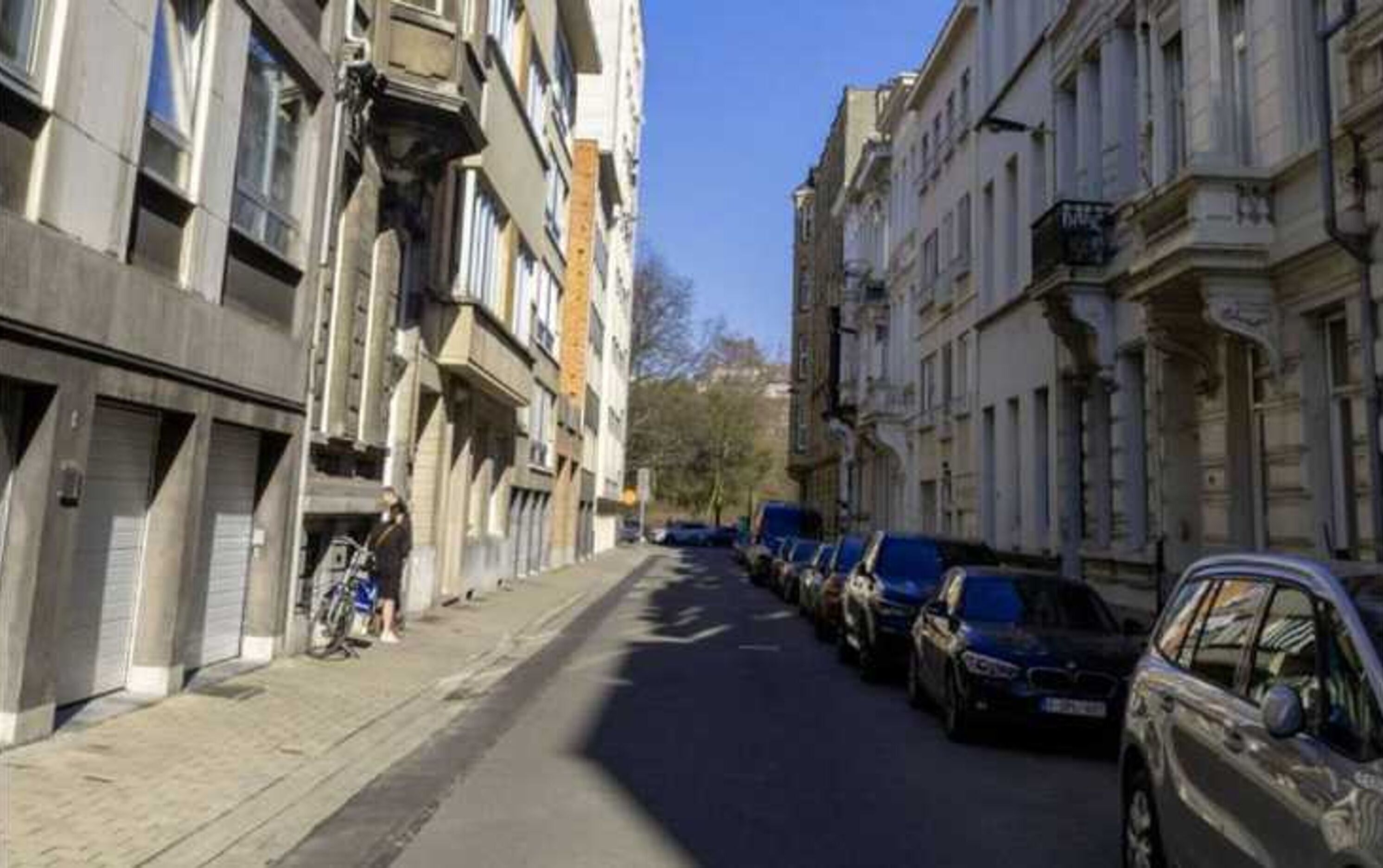 A street lined with parked cars and buildings with balconies.