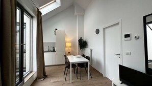 A modern kitchen with a built-in oven, a dining area with a white table and black chairs, and a TV on the right wall. - Luxury 1BR Near Fashion District by Oneluxstay (Antwerp)