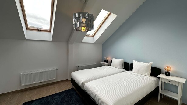 A bedroom with two beds, skylights, a radiator, and a bedside table with a lamp. - Luxury 1BR Near Fashion District by Oneluxstay (Antwerp)