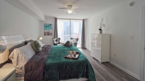 A bedroom with a bed, a ceiling fan, a window with curtains, a dresser, and a nightstand with a lamp. - Modern 1BR At Brickell Bay Club by Oneluxstay (Miami)