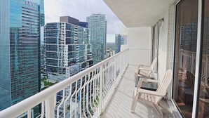 A balcony with white railings and two chairs, overlooking a cityscape with modern high-rise buildings. - Modern 1BR At Brickell Bay Club by Oneluxstay (Miami)