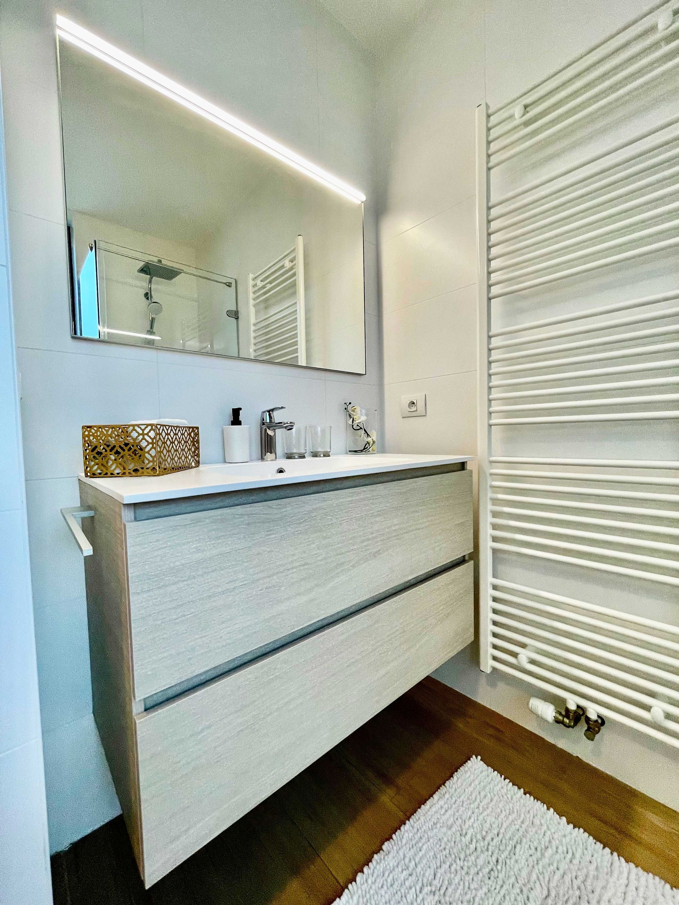 Une salle de bain moderne avec un grand miroir, un meuble-lavabo blanc et un porte-serviettes.