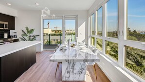 A modern kitchen with a marble countertop, a built-in microwave, and a dining area with a white table set for four. - Luxury 2BR Hollywood Pool View by Oneluxstay (Los Angeles)