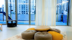 A modern living room with a large window, ottomans, a small table, and a rug with a dinosaur print. - One Lux Stay Grande Signature Residences (Dubai)