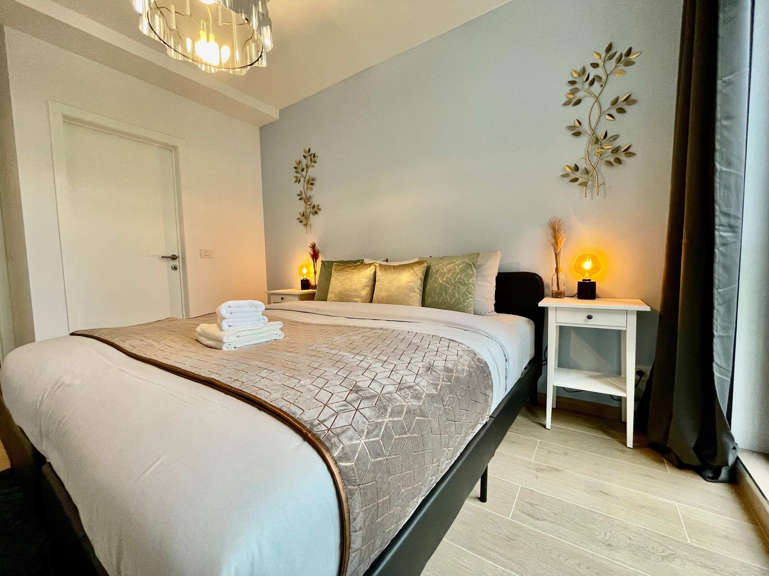 A neatly made bed with a geometric patterned bedspread, a bedside table with a lamp, and wall art.