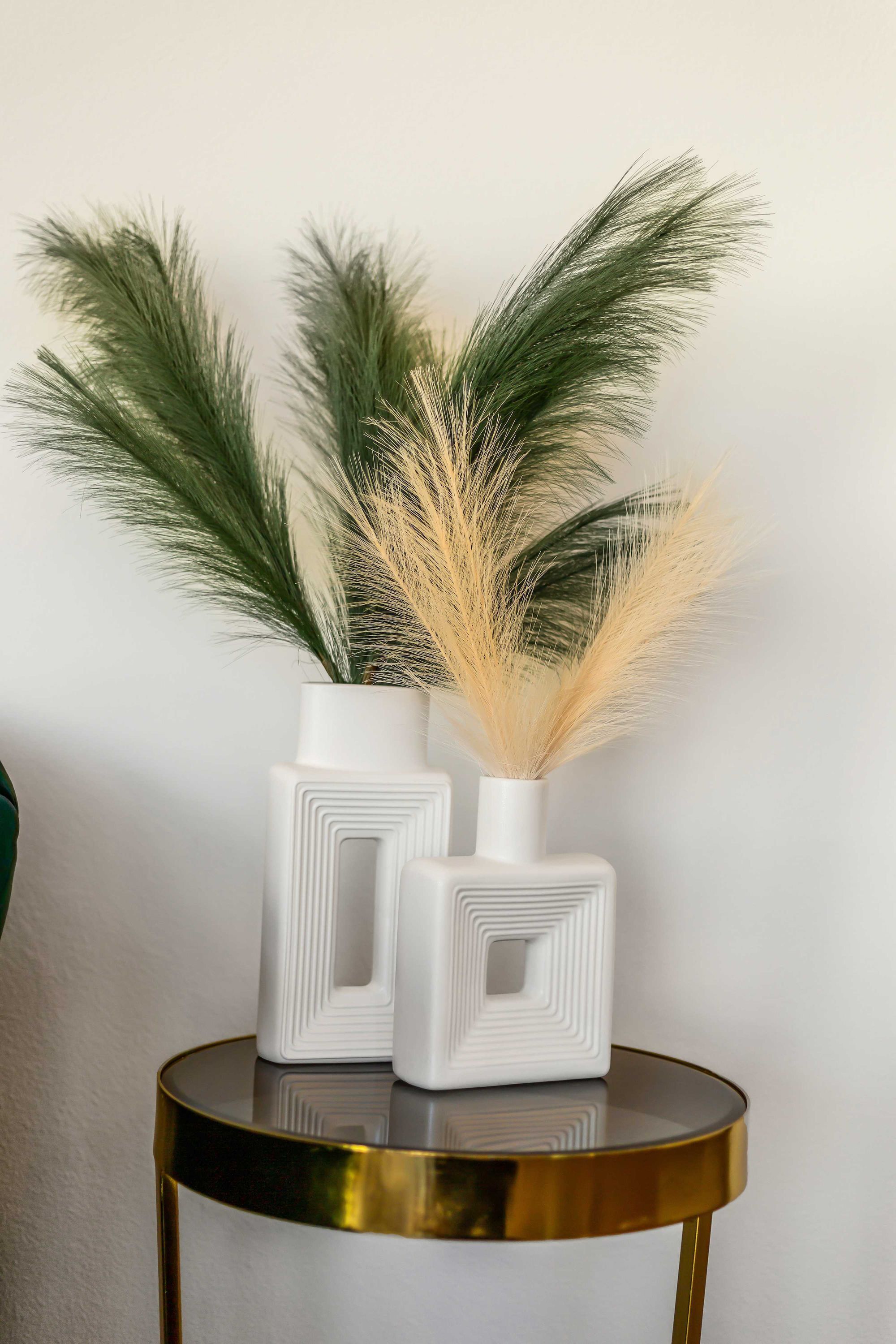 Two white vases with geometric patterns on a round table against a plain wall.