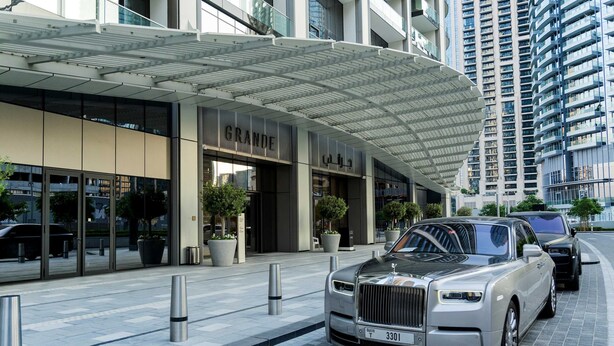 Et luksushotel med en moderne facade, en overdækket indgang og en Rolls Royce foran.