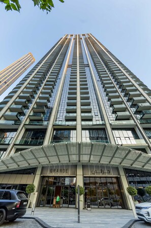 A high-rise building with a modern architectural design, featuring a prominent entrance labeled 'GRANDE,' and a clear view of the sky.