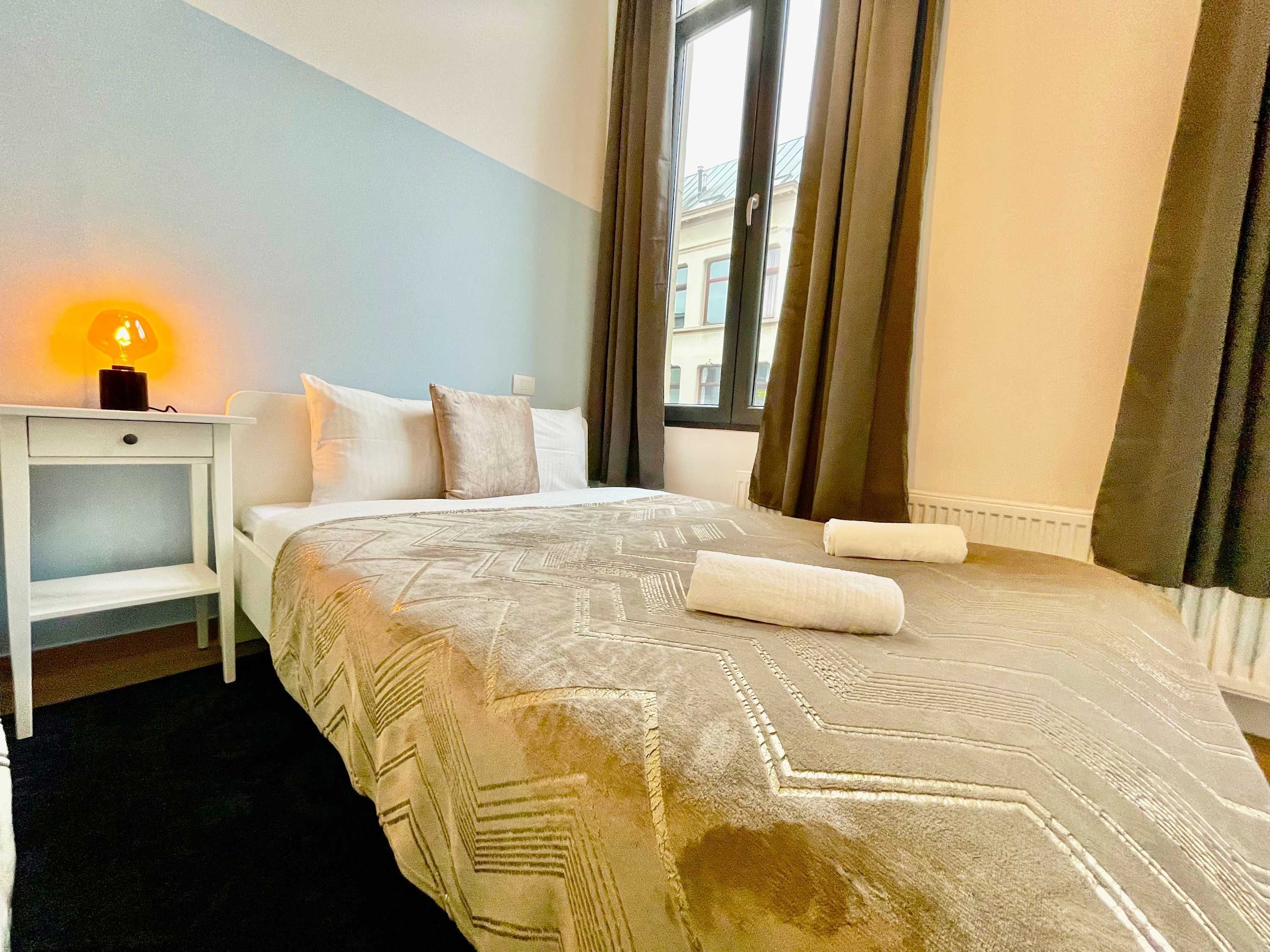 A bedroom with a bed, a nightstand, a lamp, and a window with curtains.