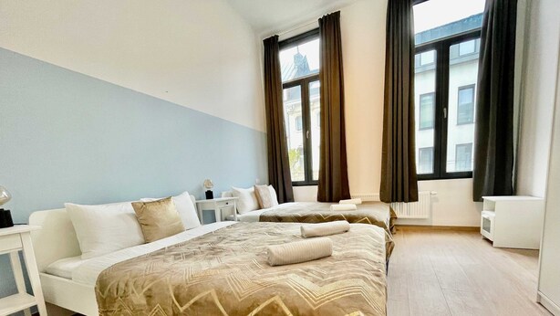A hotel room with two beds, a white sofa, a small table with a lamp, and large windows with curtains. - Luxury 2BR 1BA Near Fashion District by Oneluxstay (Antwerp)