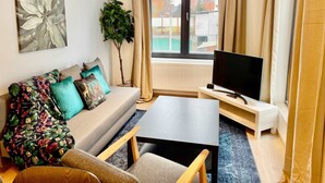 A modern living room with a sofa, a coffee table, a TV, and a large window with curtains. - Luxury 2BR 1BA Near Fashion District by Oneluxstay (Antwerp)