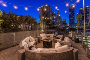 A rooftop patio with wicker furniture, string lights, and a city skyline view.