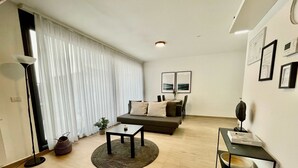 A modern living room with a sofa, coffee table, and a dining area with chairs. - Modern 1BR Near Diamond District by Oneluxstay (Antwerp)