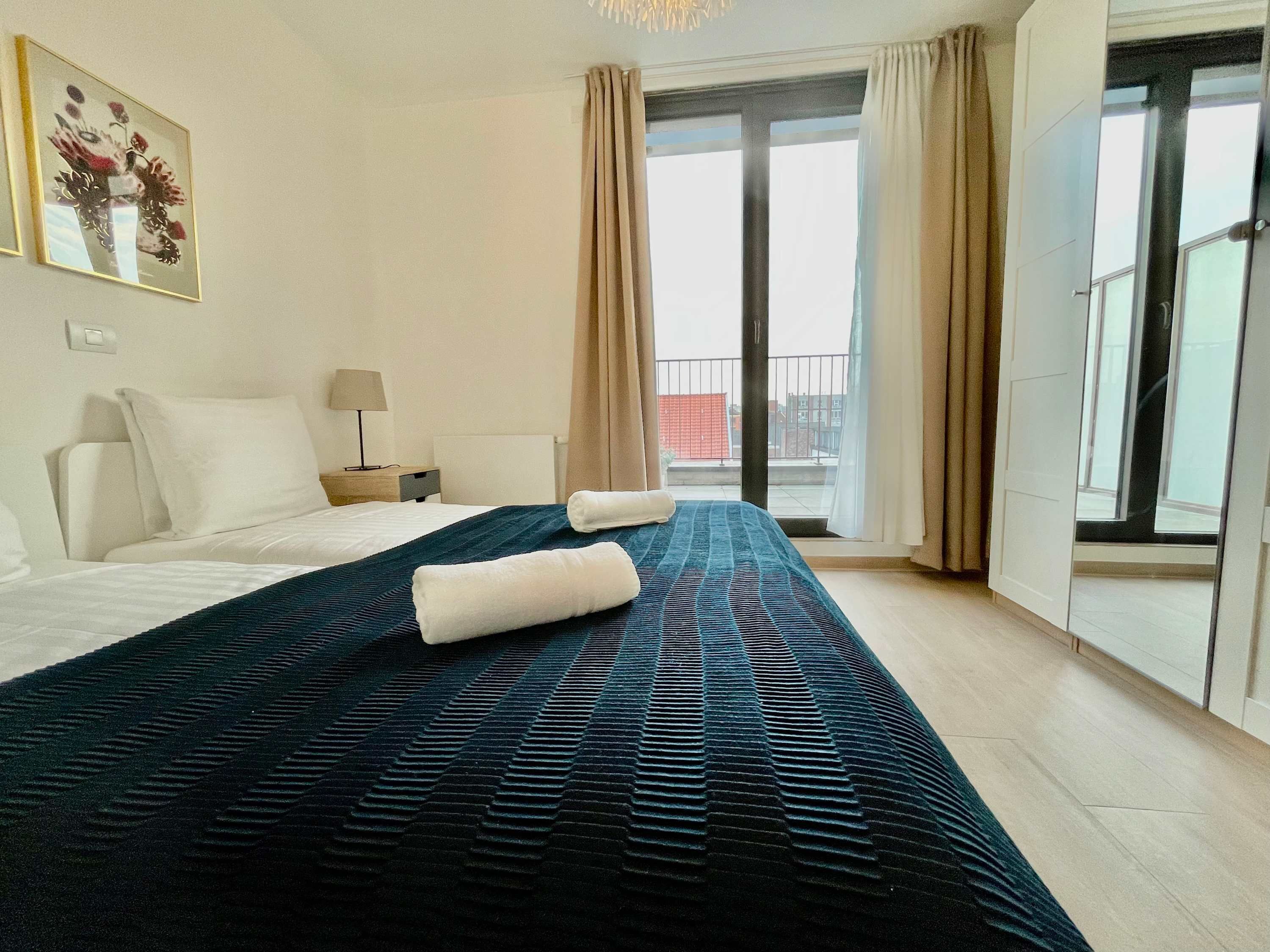 A hotel room with a bed, a nightstand, a lamp, a window with curtains, and a view of the outside.