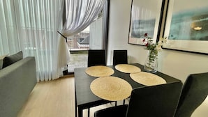 A dining area with a table set for four, featuring woven placemats, black chairs, and a vase with flowers. - Modern 1BR Near Diamond District by Oneluxstay (Antwerp)